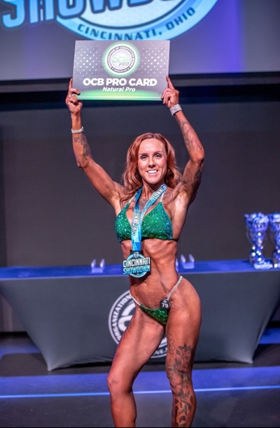 Bikini competitor holding a pro card after winning a show